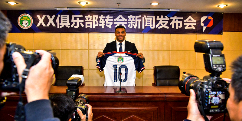 足球运动员转会新闻发布会现场，球员手持新球队球衣